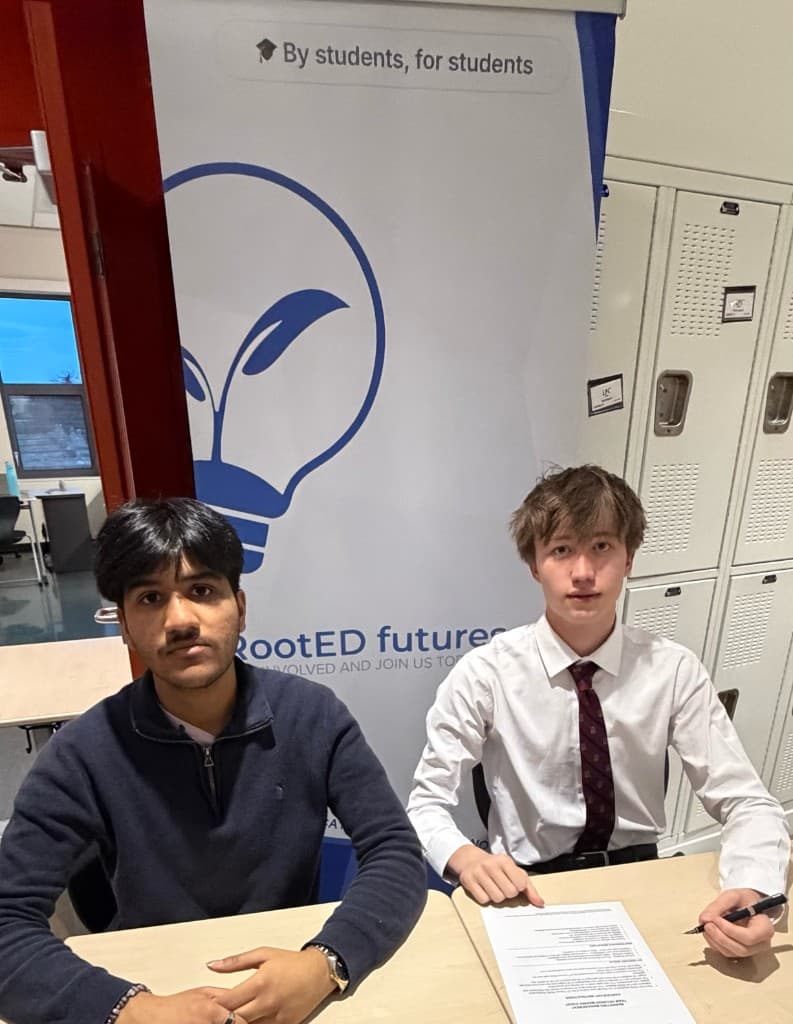 Two RootED futures student leaders seated at a table in front of a RootED futures banner
