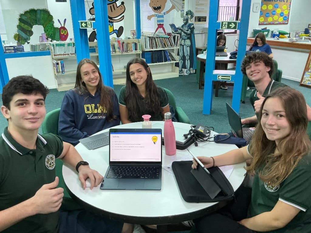 Five high school students collaborating around a table with a RootED futures lesson on a laptop